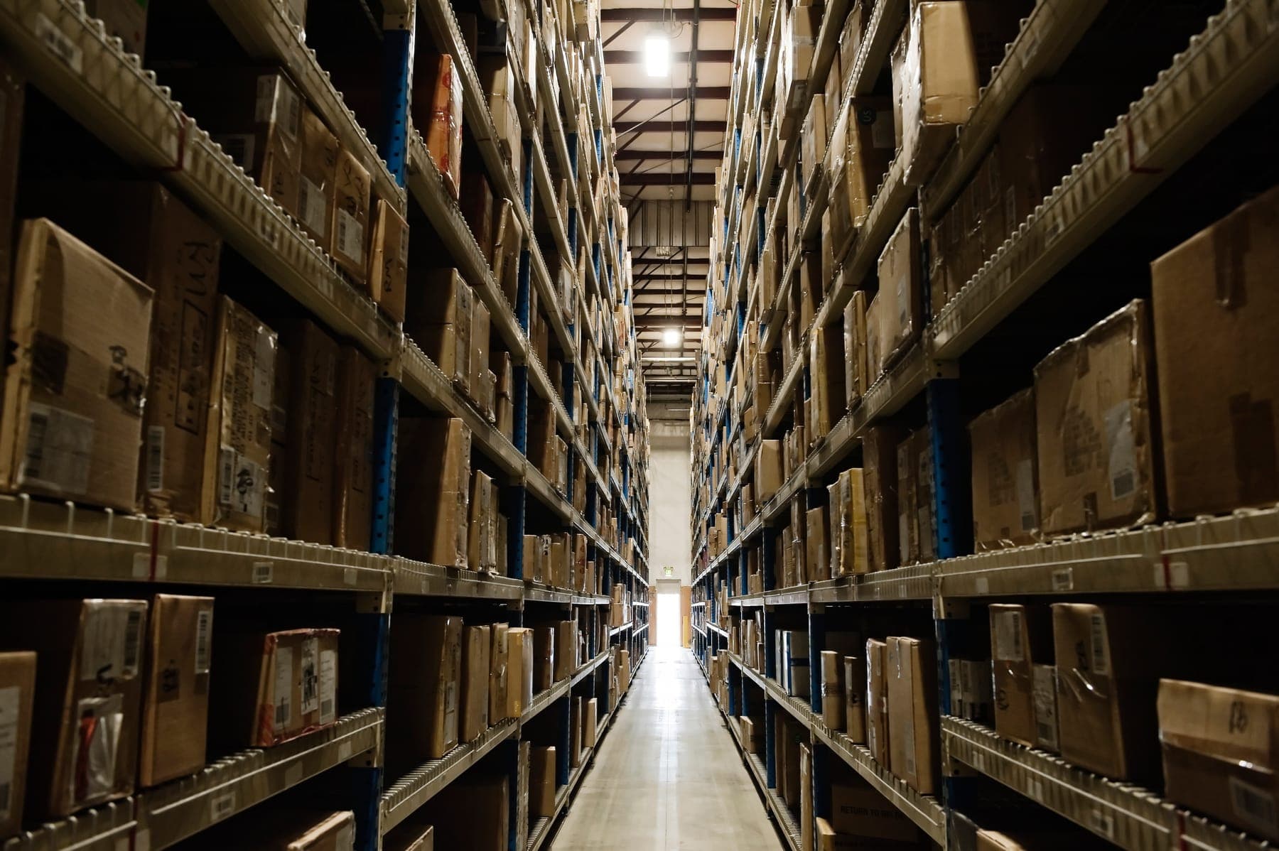 A warehouse aisle between tall shelves of boxed inventory